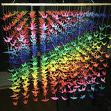 An installation of rainbow coloured paper cranes suspended in the shape of a cube.